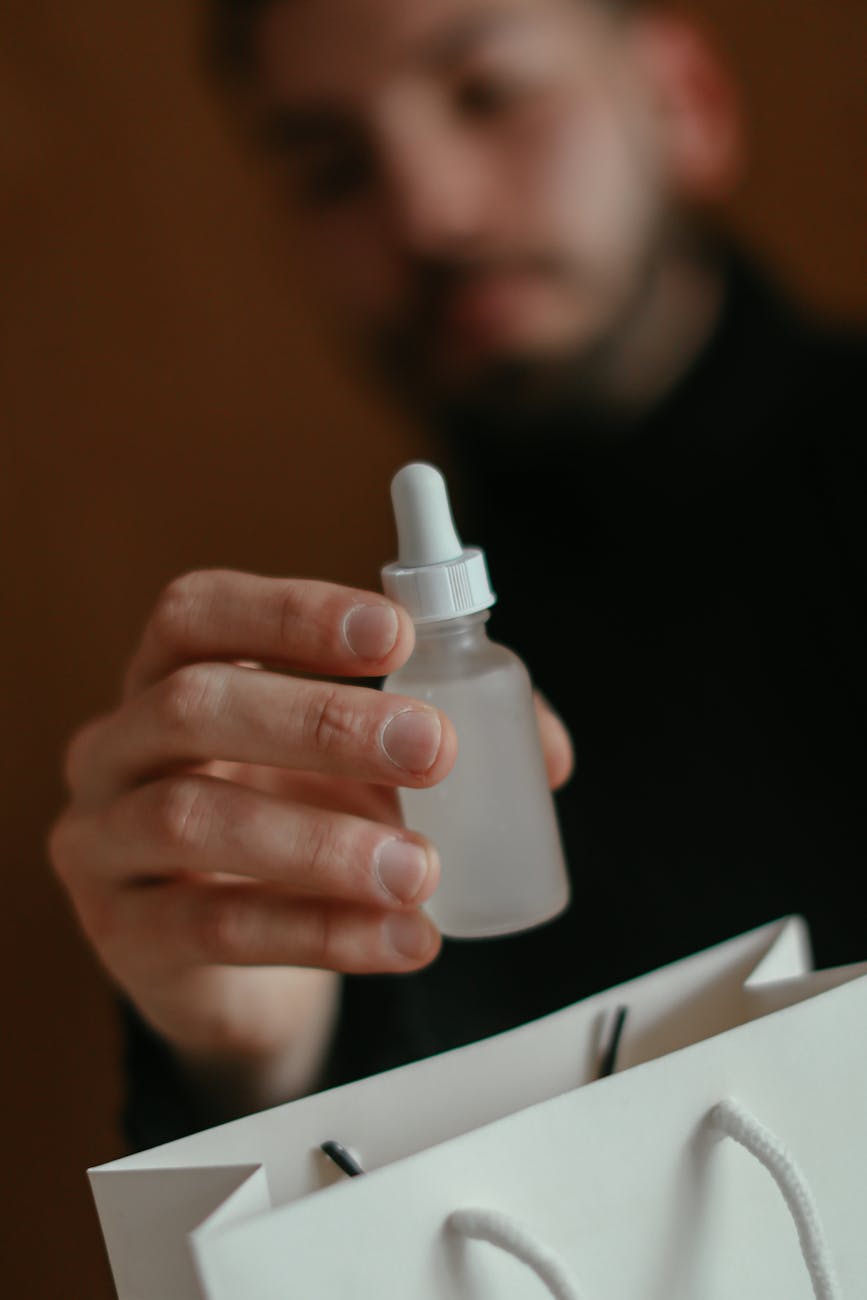 crop young man showing bottle of skin care product