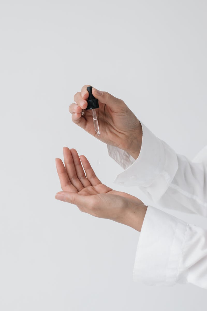 A person's hands applying skincare serum using a dropper for a beauty routine.